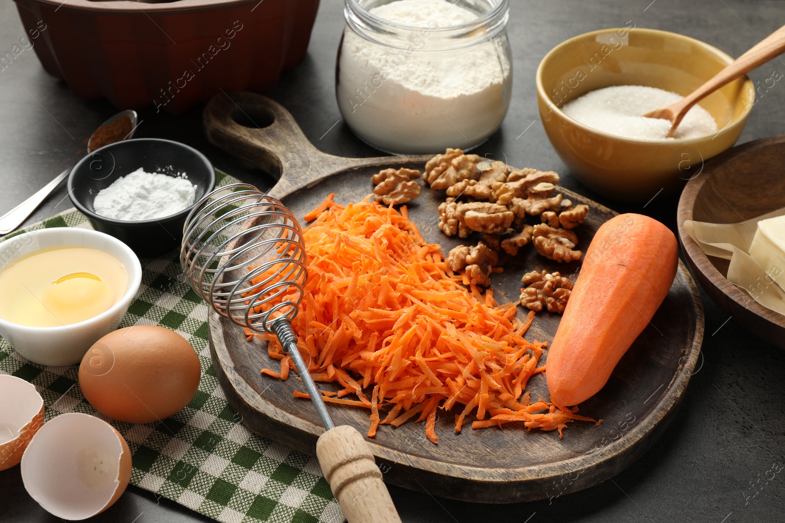 Photo of Different ingredients for making carrot cake and whisk on dark textured table, closeup