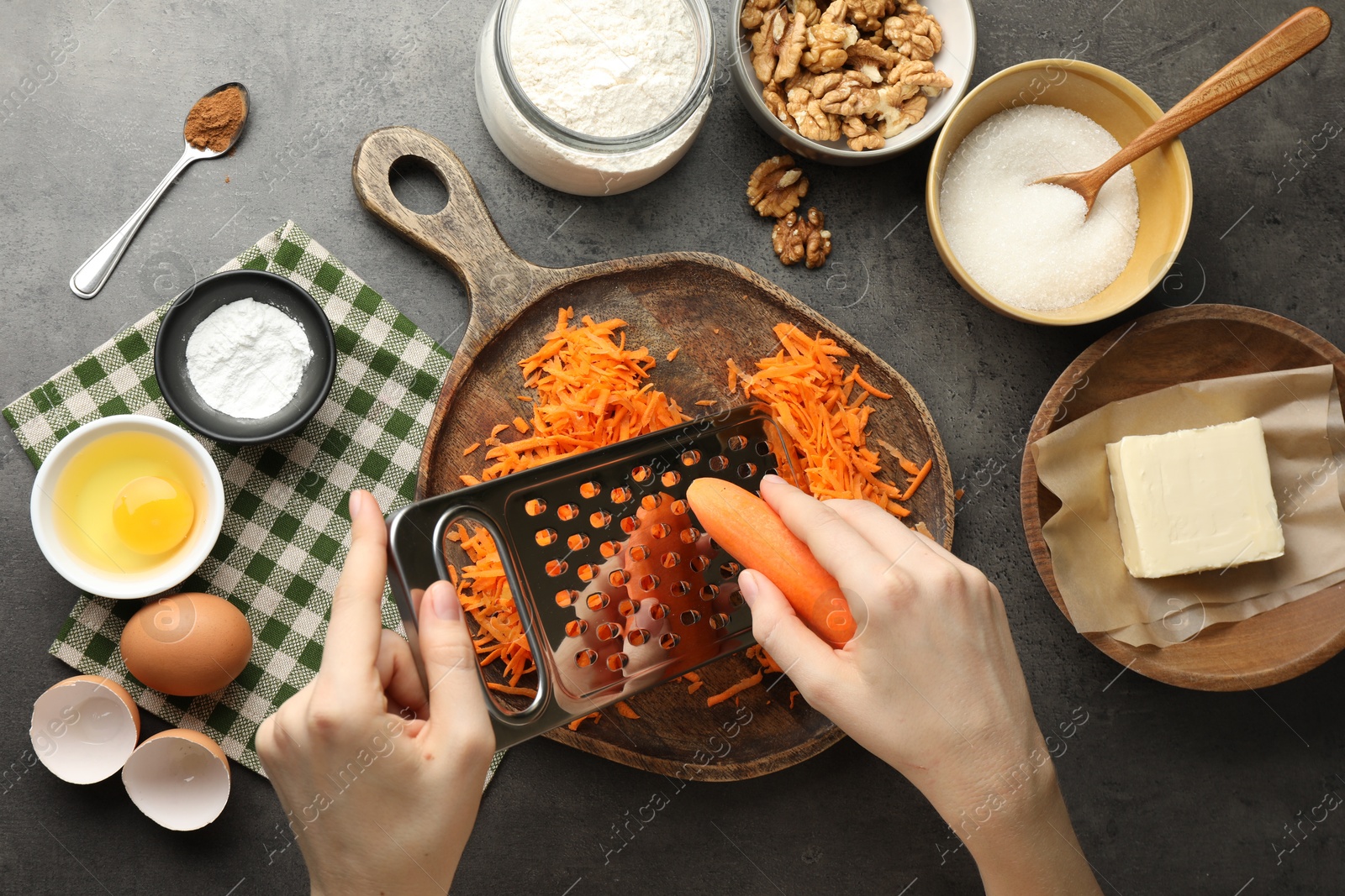 Photo of Making carrot cake. Woman grating vegetable at dark textured table with ingredients, top view