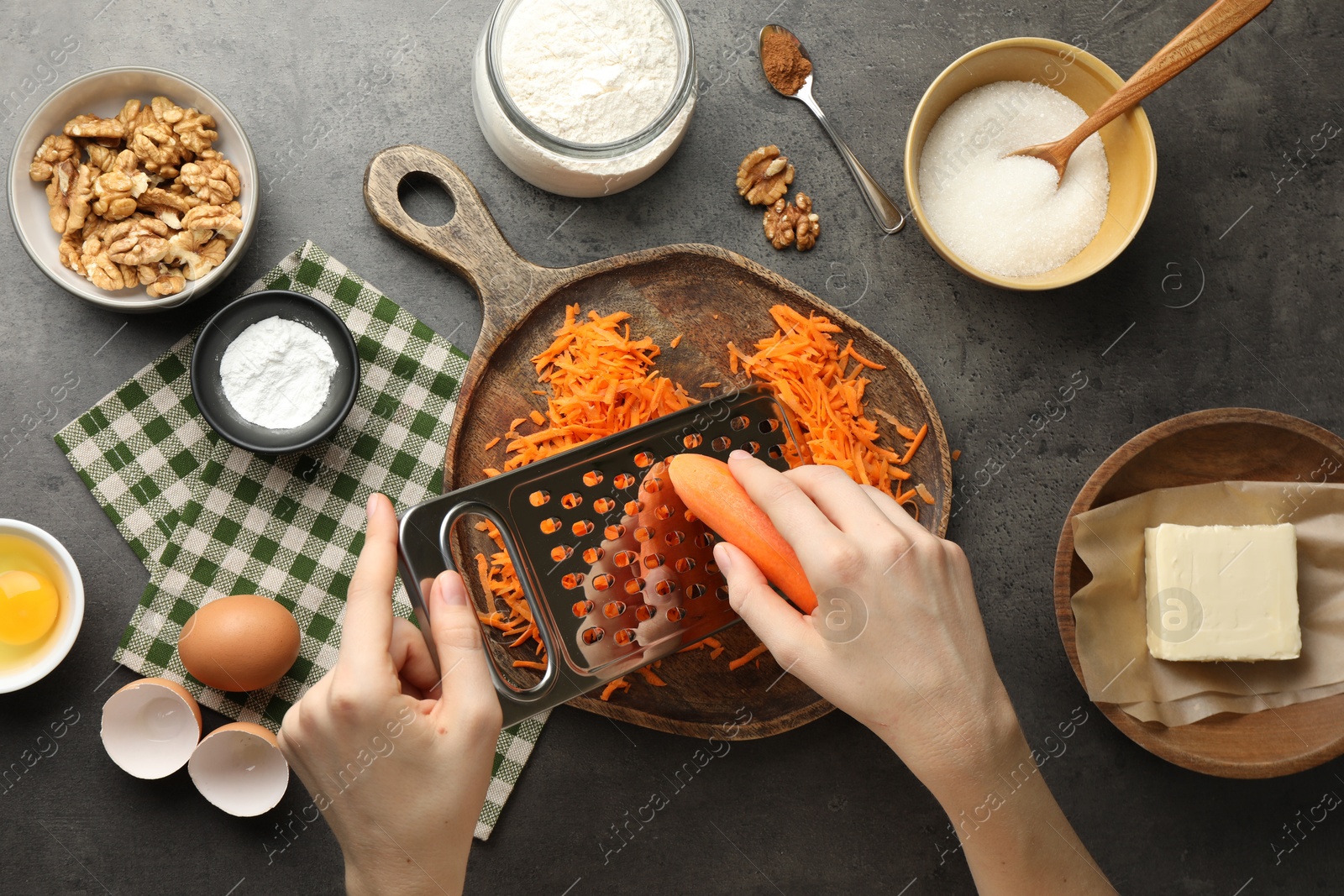 Photo of Making carrot cake. Woman grating vegetable at dark textured table with ingredients, top view