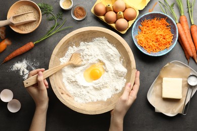 Photo of Woman making dough for carrot cake at dark textured table with ingredients, top view