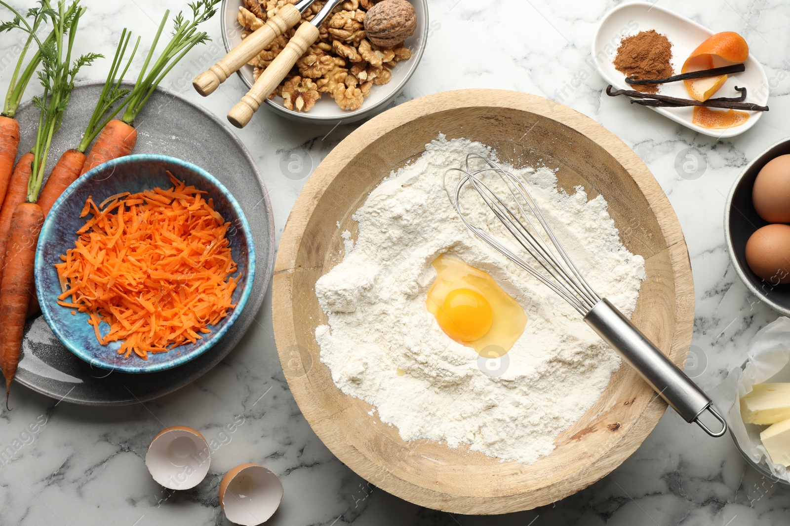 Photo of Making carrot cake. Different ingredients for dough and kitchenware on white marble table, flat lay