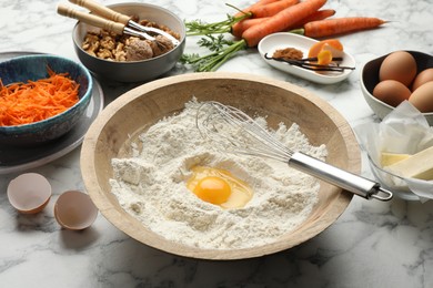 Photo of Making carrot cake. Bowl with flour, egg, whisk and other ingredients on white marble table, closeup