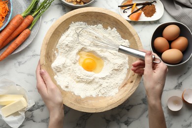 Photo of Woman making dough for carrot cake at white marble table with ingredients, top view