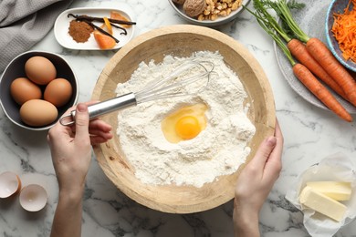 Photo of Woman making dough for carrot cake at white marble table with ingredients, top view