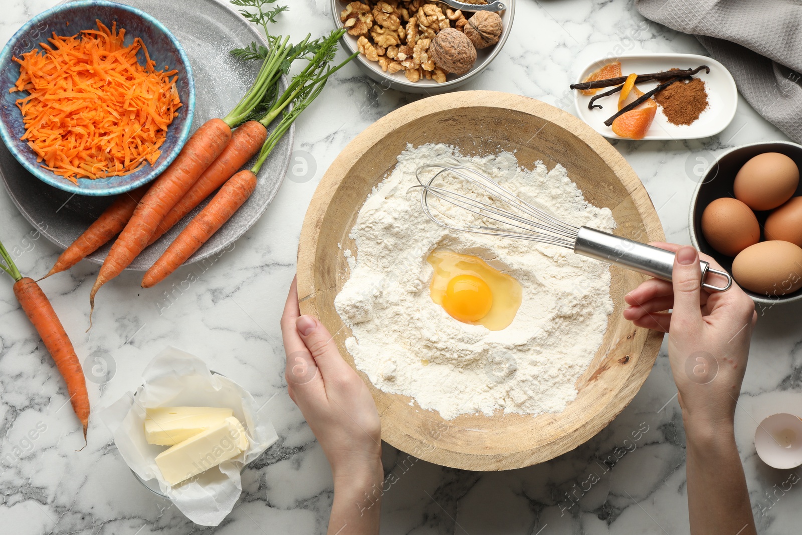 Photo of Woman making dough for carrot cake at white marble table with ingredients, top view