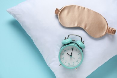 Photo of Time for sleeping. Alarm clock, sleep mask and pillow on light blue background, top view. Space for text