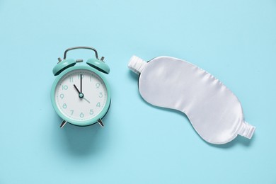 Photo of Alarm clock and sleep mask on light blue background, flat lay. Time for sleeping