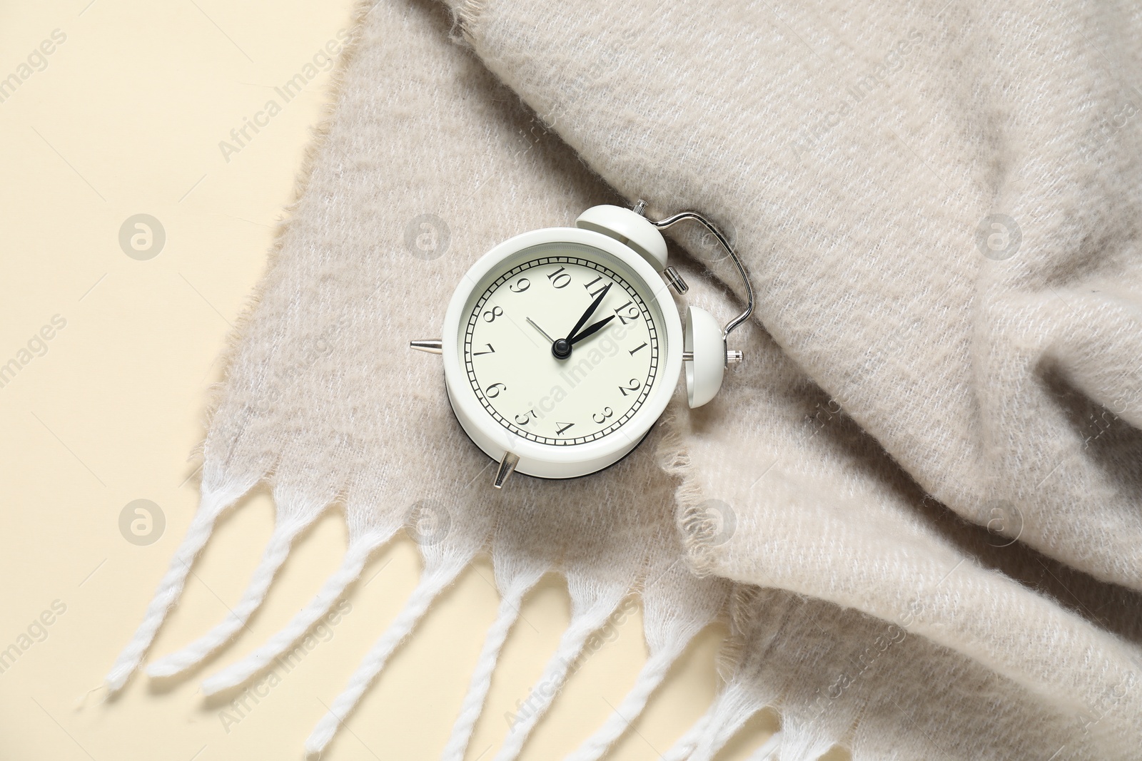 Photo of Alarm clock and blanket on beige background, top view. Time for sleeping