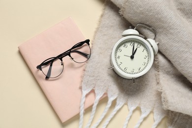 Photo of Alarm clock, glasses, book and blanket on beige background, flat lay. Time for knowledge