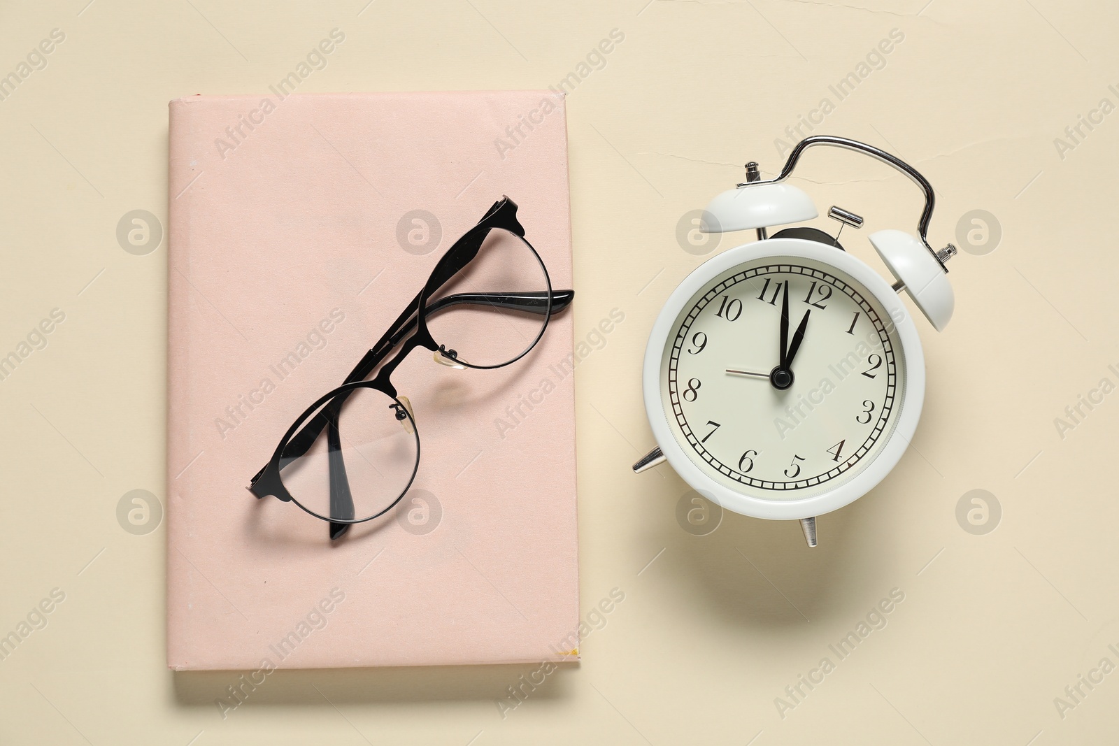 Photo of Alarm clock, glasses and book on beige background, flat lay. Time for knowledge