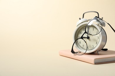 Photo of Alarm clock, glasses and book on beige background, space for text. Time for knowledge