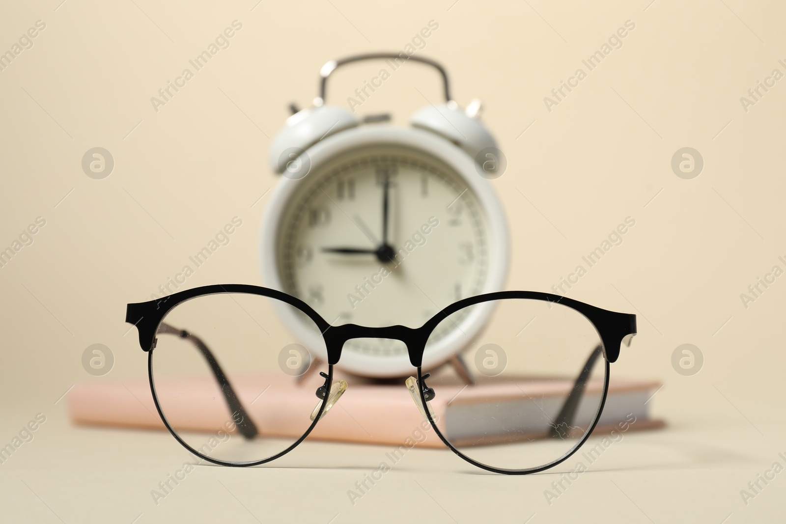 Photo of Alarm clock, glasses and book on beige background, selective focus. Time for knowledge