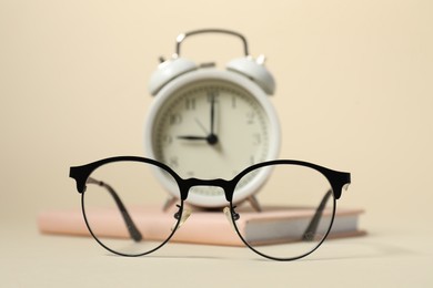 Photo of Alarm clock, glasses and book on beige background, selective focus. Time for knowledge