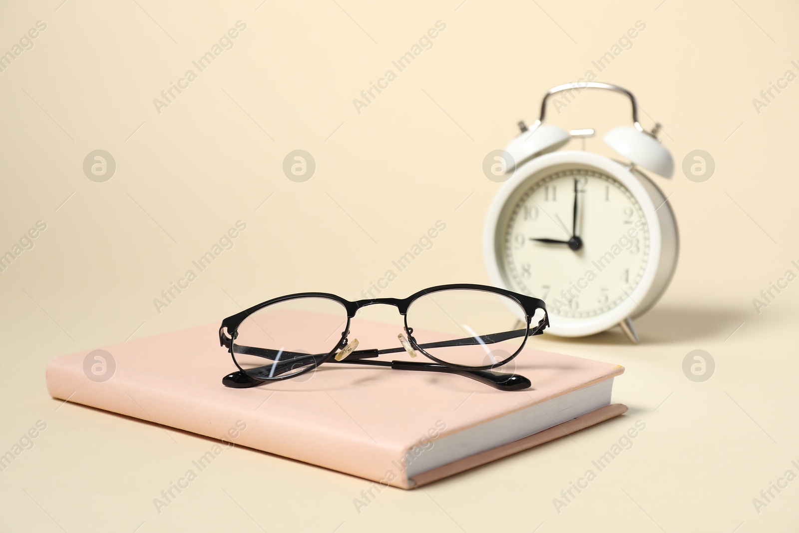 Photo of Alarm clock, glasses and book on beige background, closeup. Time for knowledge