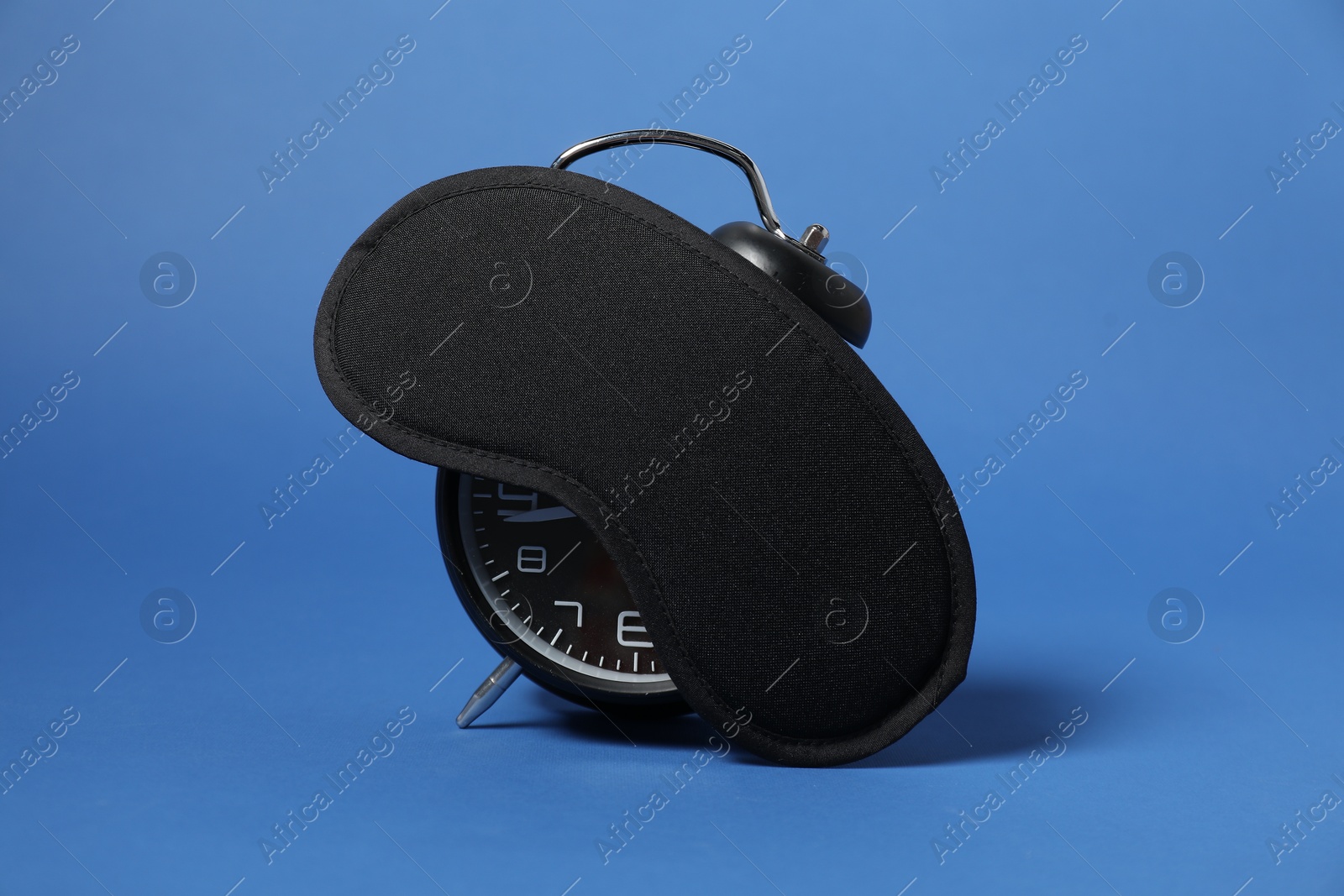 Photo of Alarm clock and sleep mask on blue background. Time for sleeping