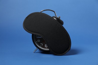 Photo of Alarm clock and sleep mask on blue background. Time for sleeping