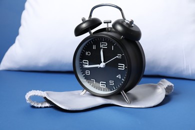 Photo of Alarm clock, sleep mask and pillow on blue background. Time for sleeping