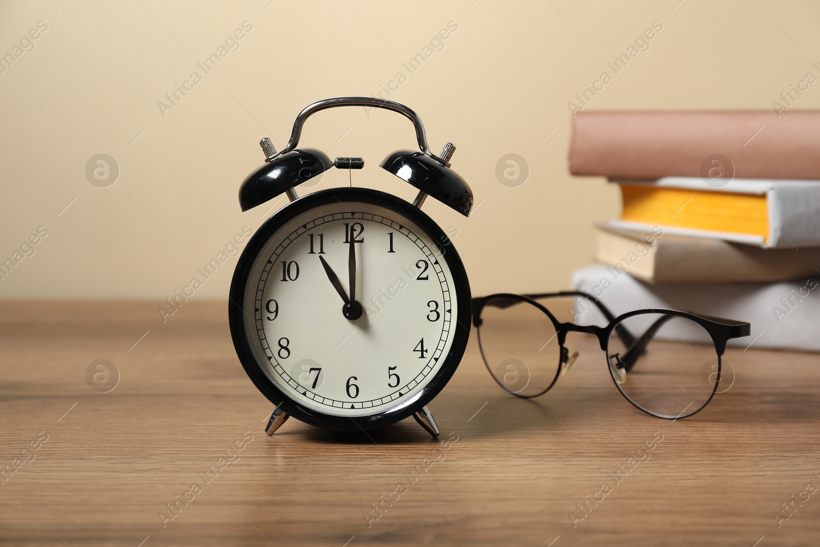 Photo of Alarm clock, glasses and stacked books on wooden table. Time for knowledge