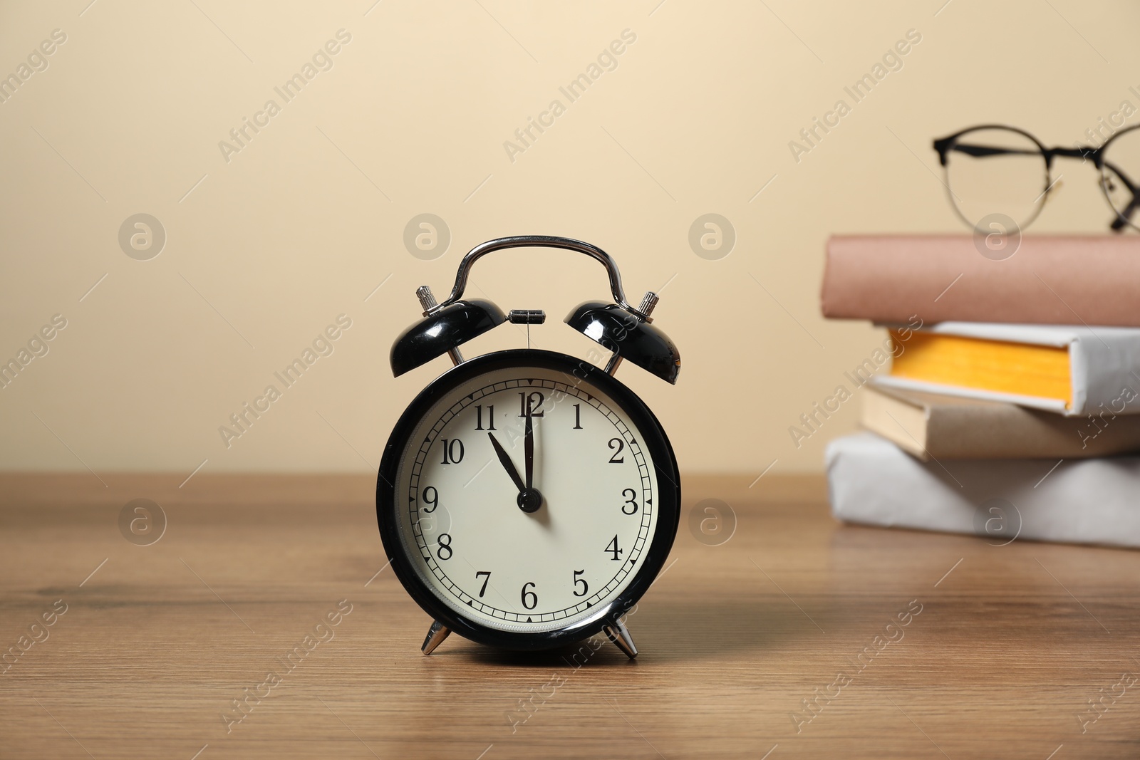 Photo of Alarm clock, glasses and stacked books on wooden table. Time for knowledge