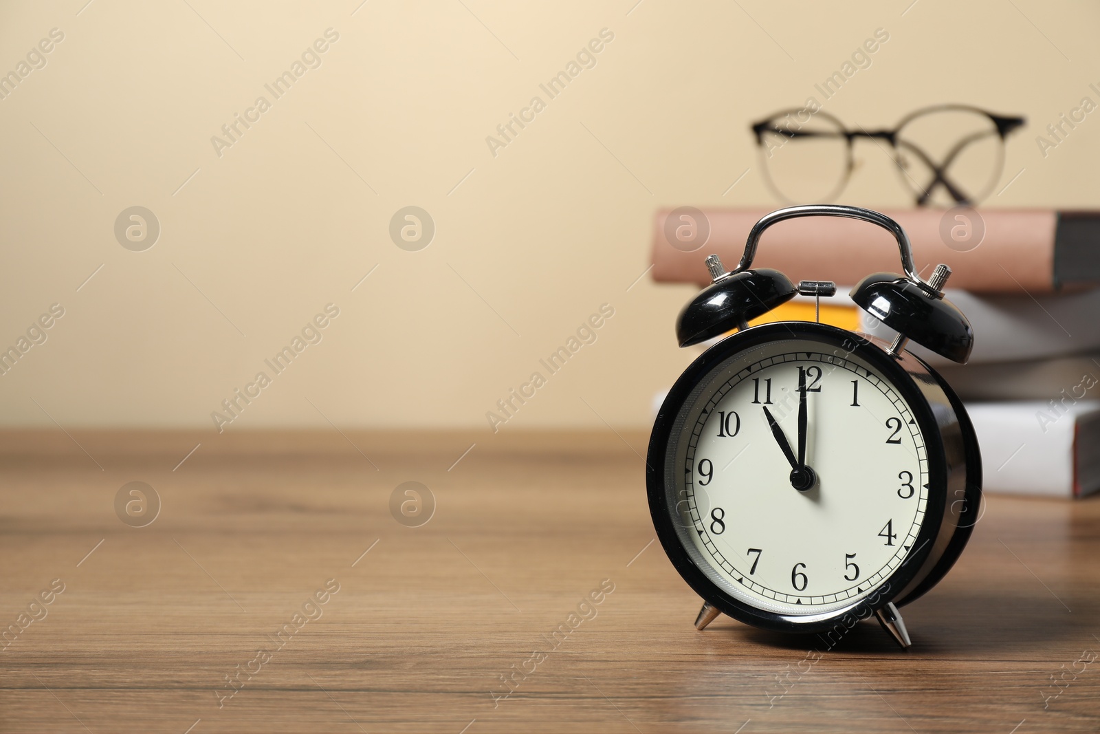 Photo of Alarm clock, glasses and stacked books on wooden table, space for text. Time for knowledge