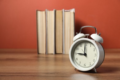 Photo of Alarm clock and books on wooden table, space for text. Time for knowledge