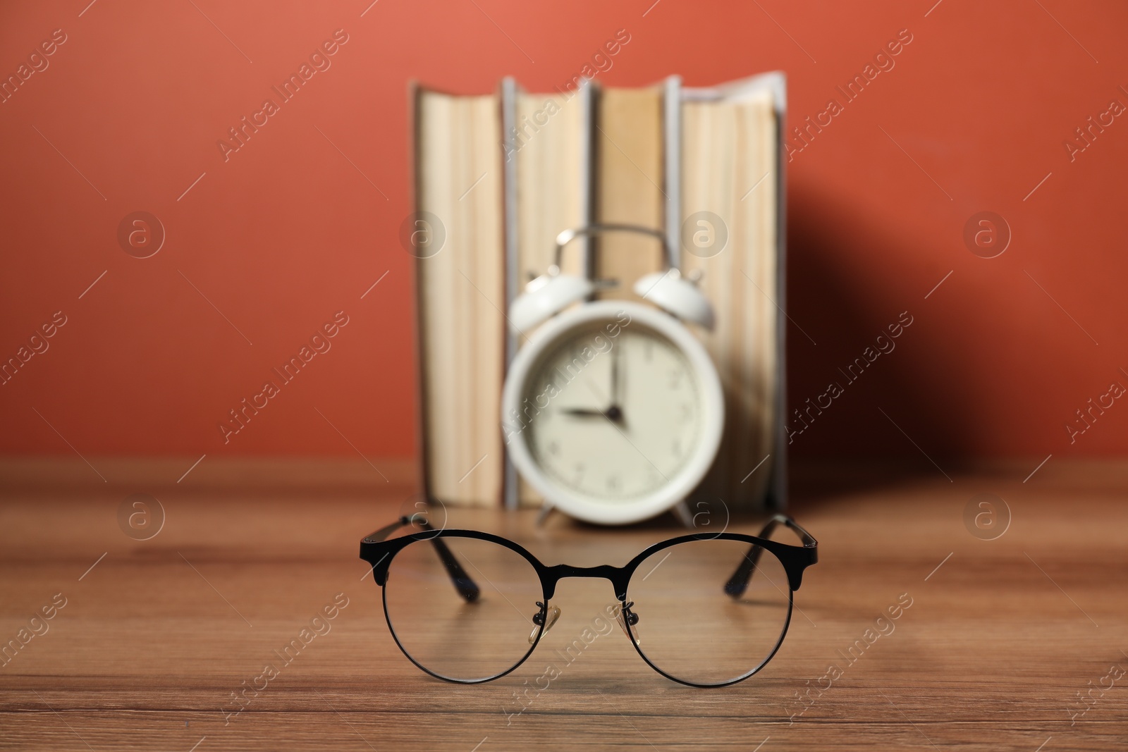 Photo of Alarm clock, glasses and books on wooden table, selective focus. Time for knowledge