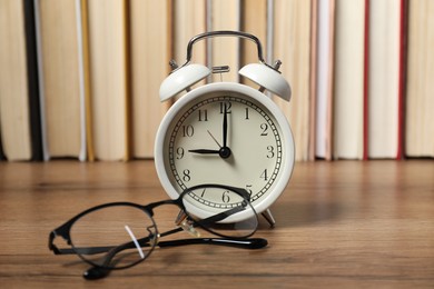 Photo of Alarm clock, glasses and books on wooden table, space for text. Time for knowledge