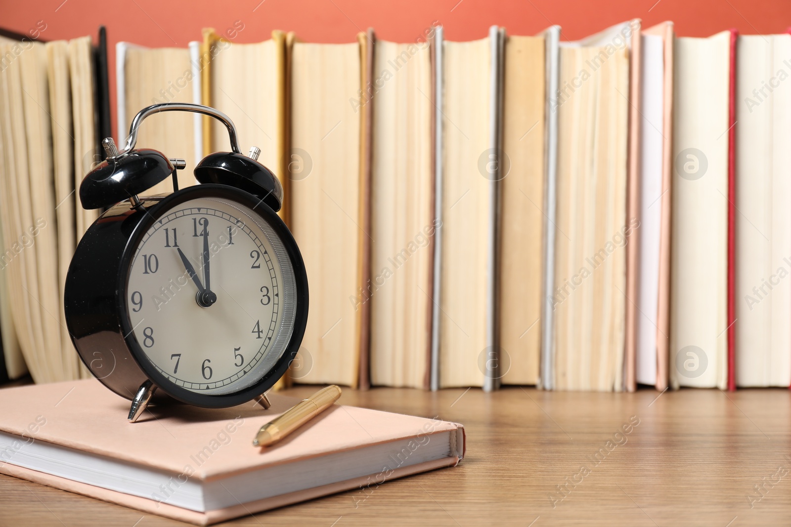 Photo of Alarm clock, books and pen on wooden table, space for text. Time for knowledge