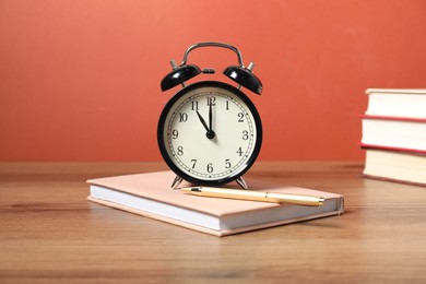 Photo of Alarm clock, books and pen on wooden table. Time for knowledge