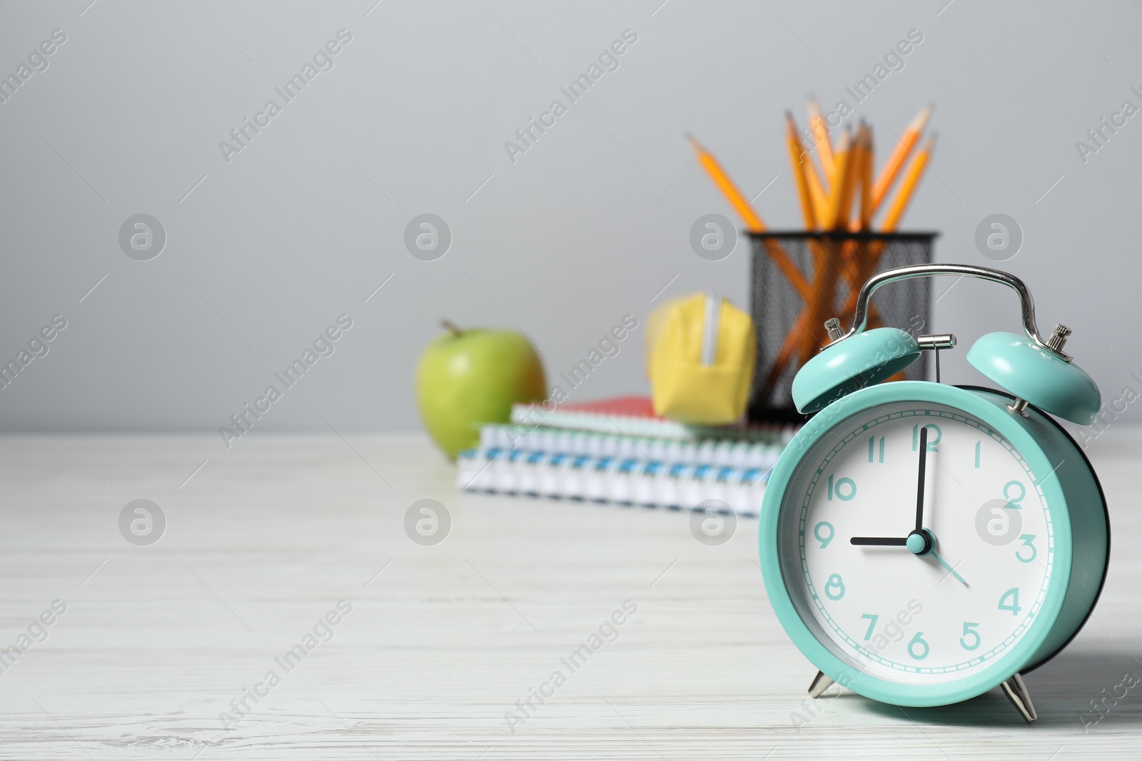 Photo of Alarm clock, stationery and apple on white wooden table, space for text. Time for knowledge