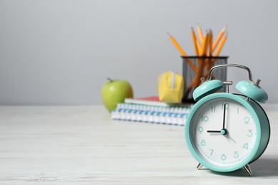 Photo of Alarm clock, stationery and apple on white wooden table, space for text. Time for knowledge