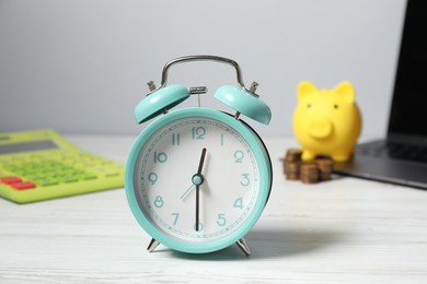 Photo of Alarm clock, coins, calculator, laptop and piggy bank on white wooden table. Tax time