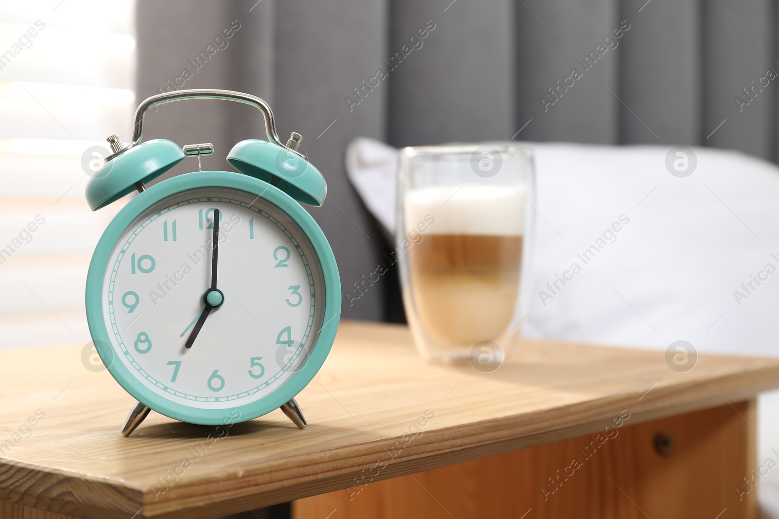 Photo of Alarm clock and coffee on nightstand near bed