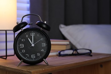 Photo of Alarm clock, books and glasses on nightstand near bed. Space for text