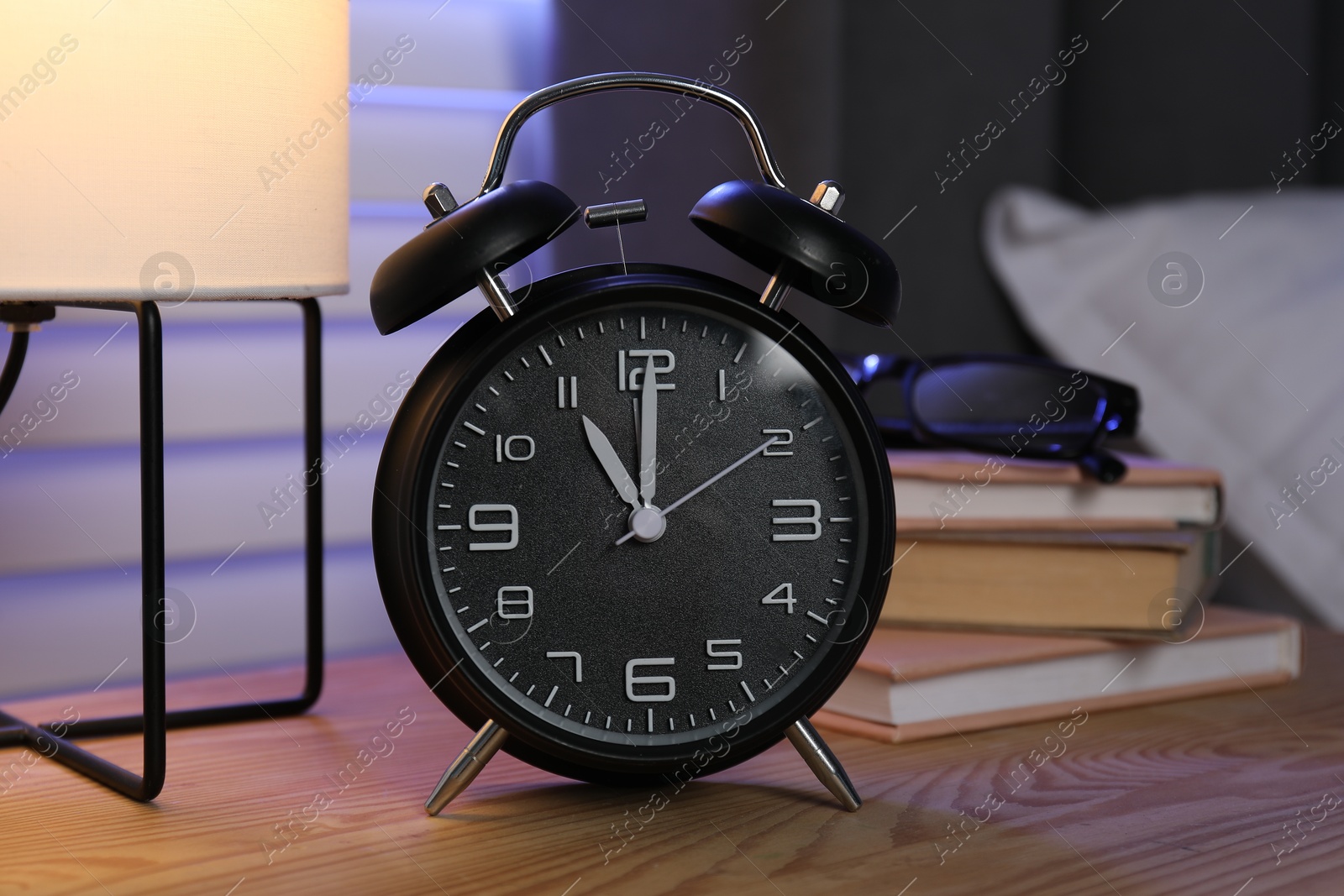 Photo of Alarm clock, books and glasses on nightstand near bed