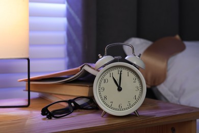 Photo of Alarm clock, books and glasses on nightstand near bed