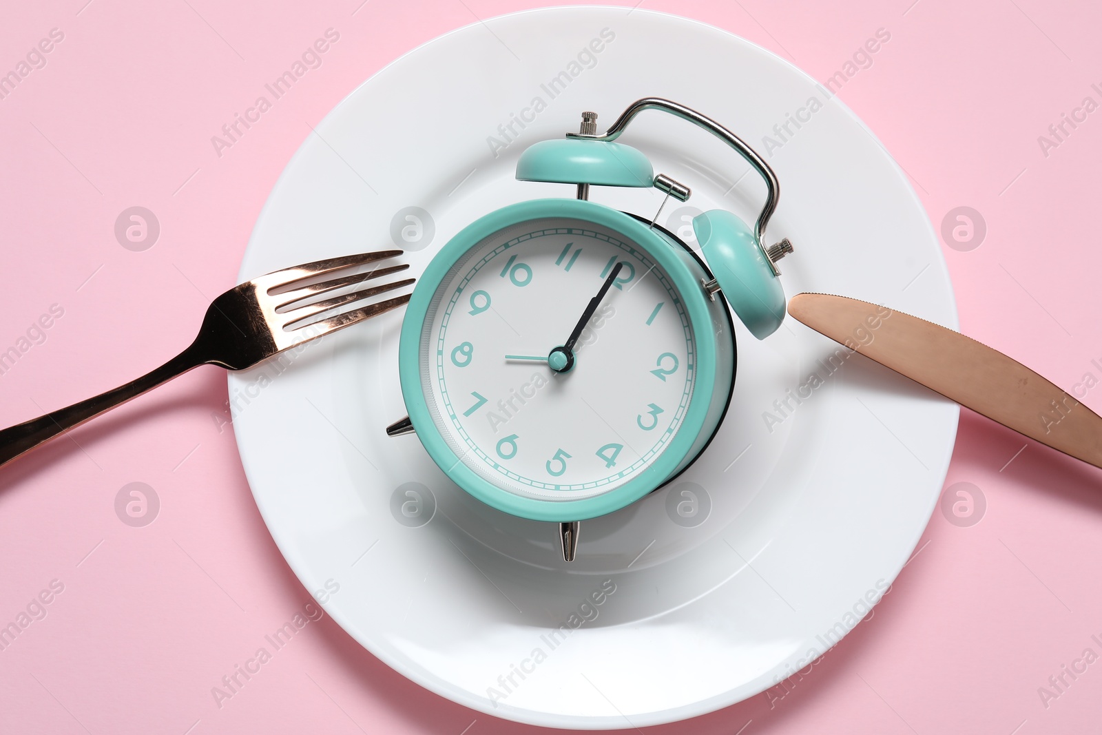 Photo of Alarm clock, plate and cutlery on pink background, flat lay