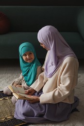 Muslim woman and her daughter with Quran praying on mat at home