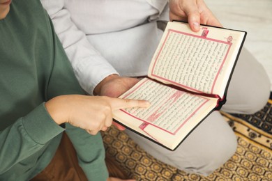 Muslim man and his son reading Quran at home, closeup