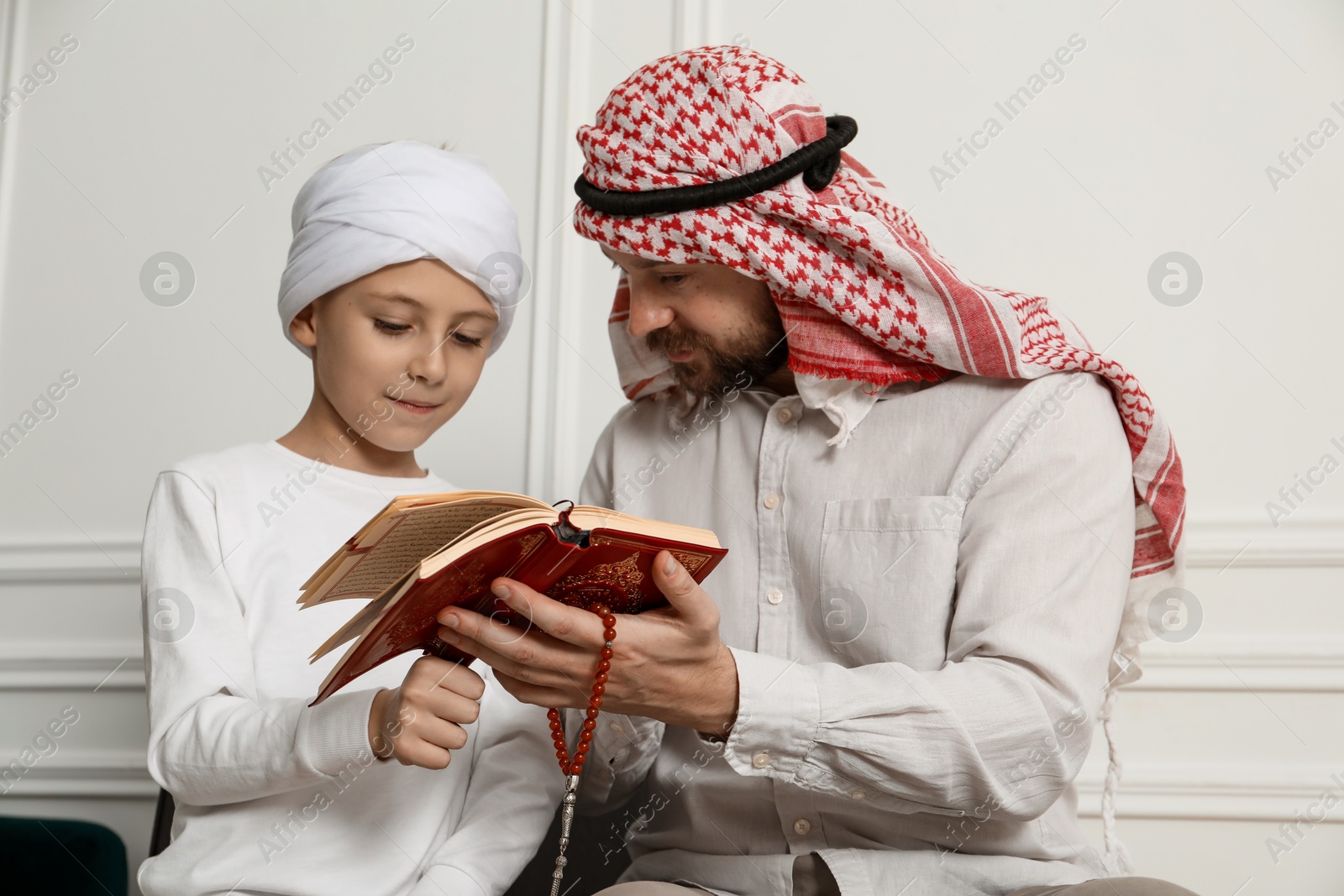 Photo of Muslim man and his son reading Quran at home