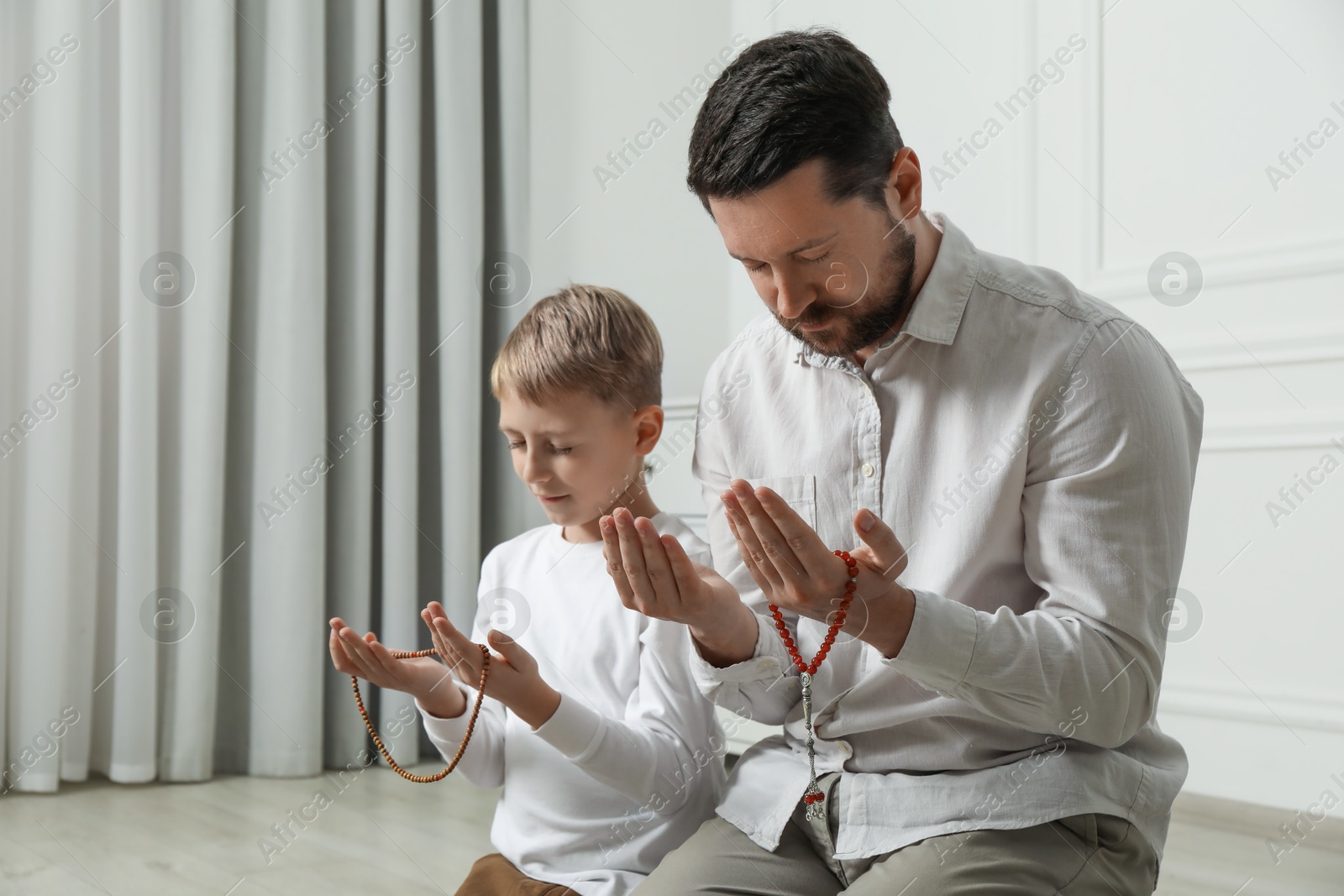 Photo of Muslim man and his son with beads praying indoors