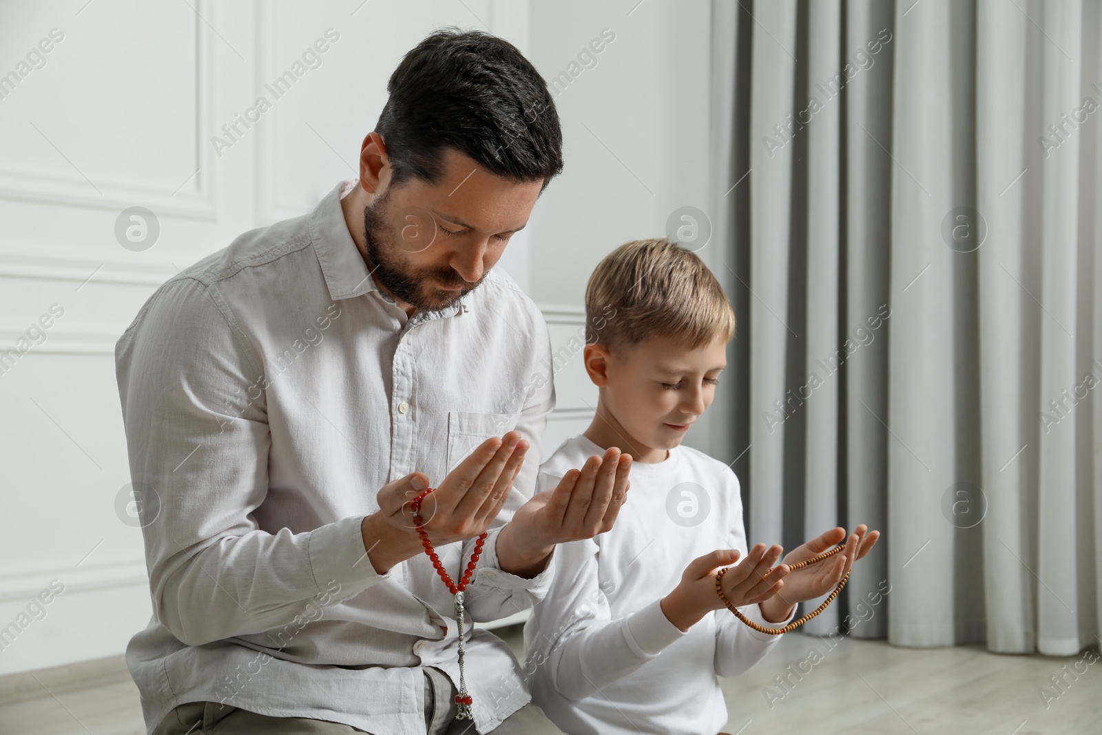 Photo of Muslim man and his son with beads praying indoors