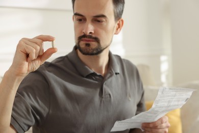 Man with pill and medical instruction at home, selective focus