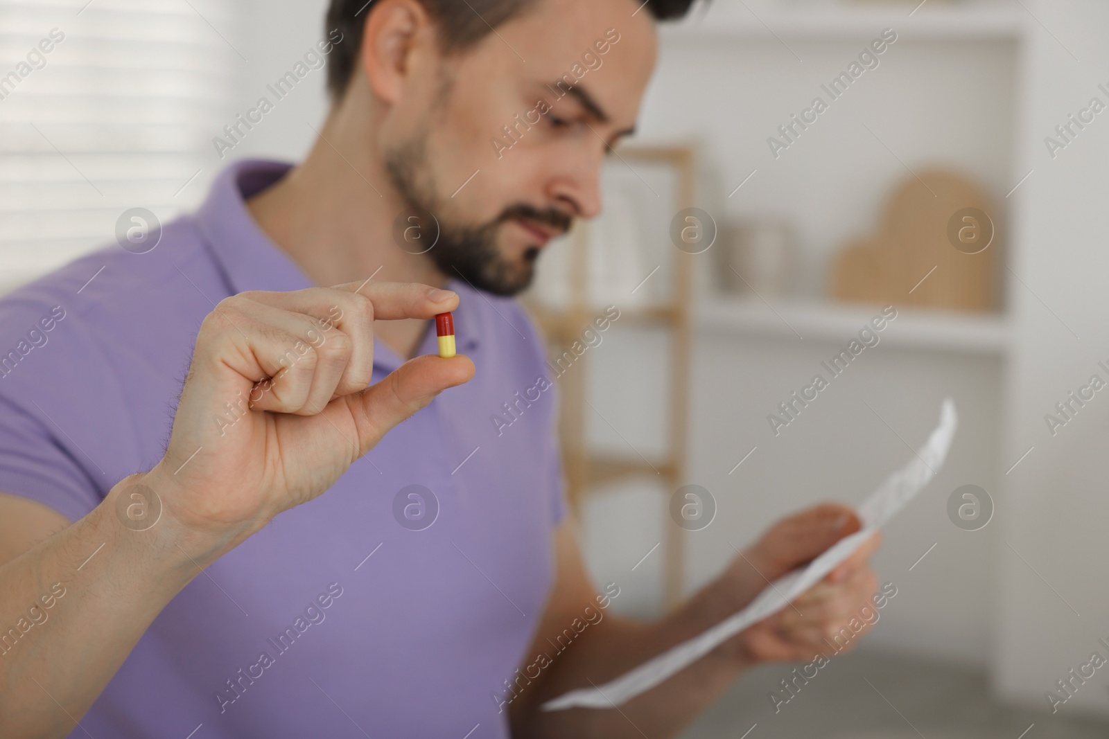 Photo of Man with pill reading instruction at home, selective focus