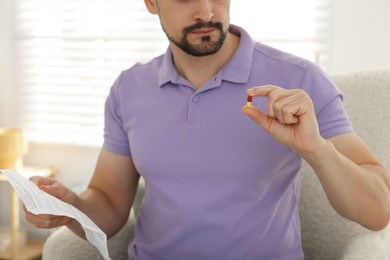 Photo of Man with pill and medical instruction at home, closeup