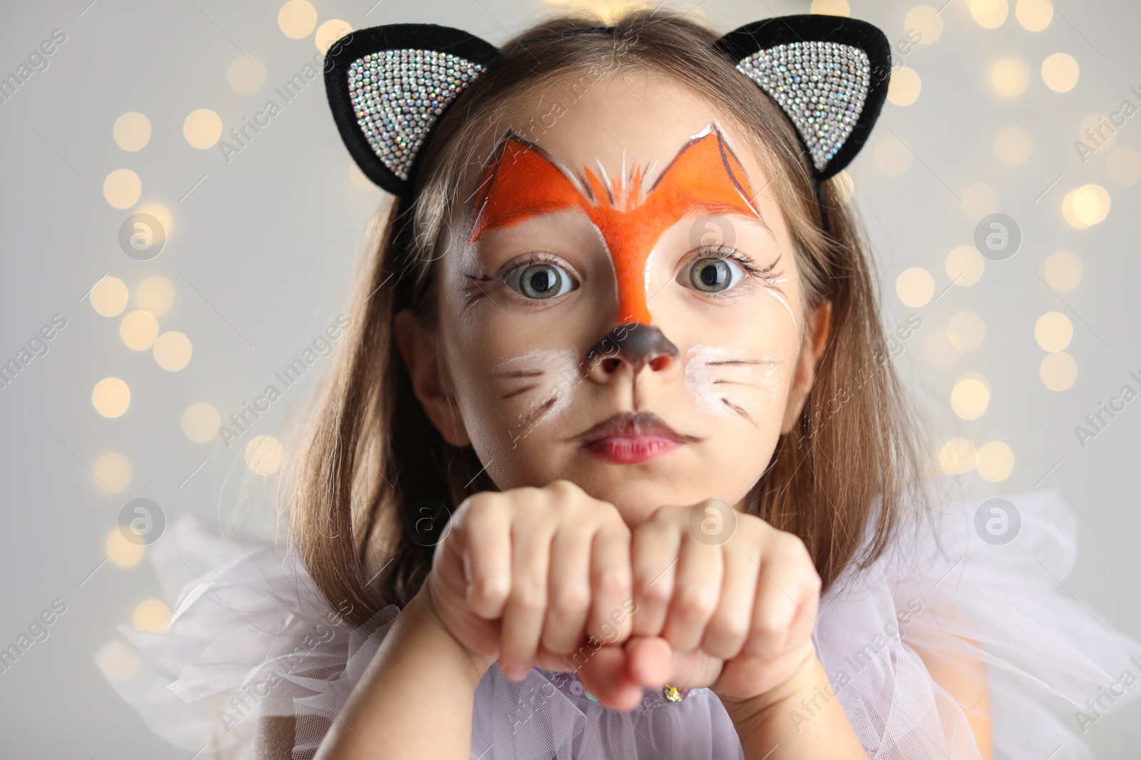 Photo of Cute girl with painted face and ears as cat on grey background with blurred lights