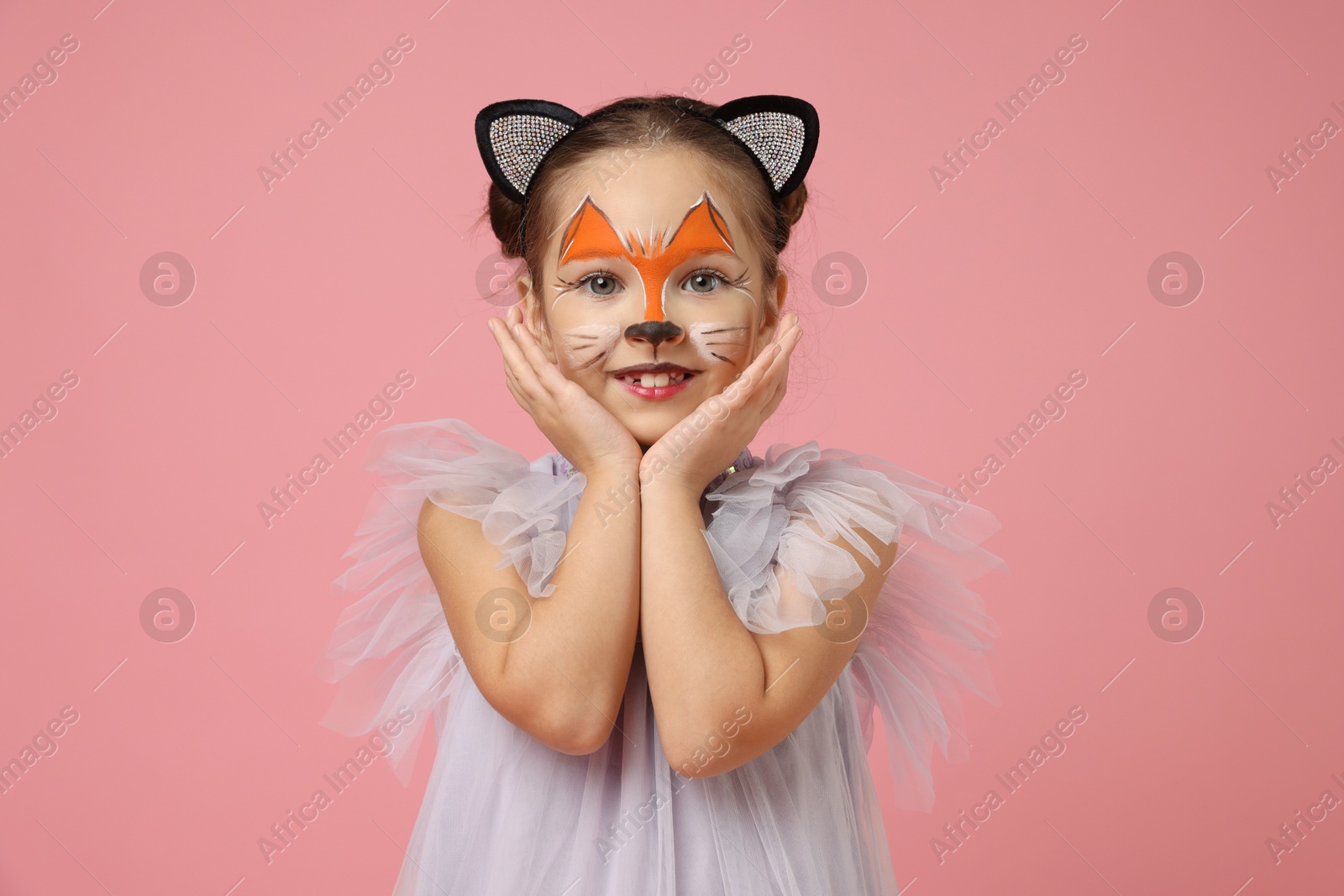 Photo of Cute girl with painted face and ears as cat on pink background