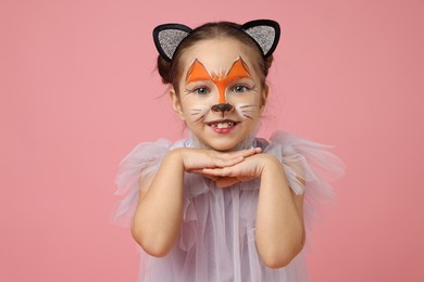 Photo of Cute girl with painted face and ears as cat on pink background