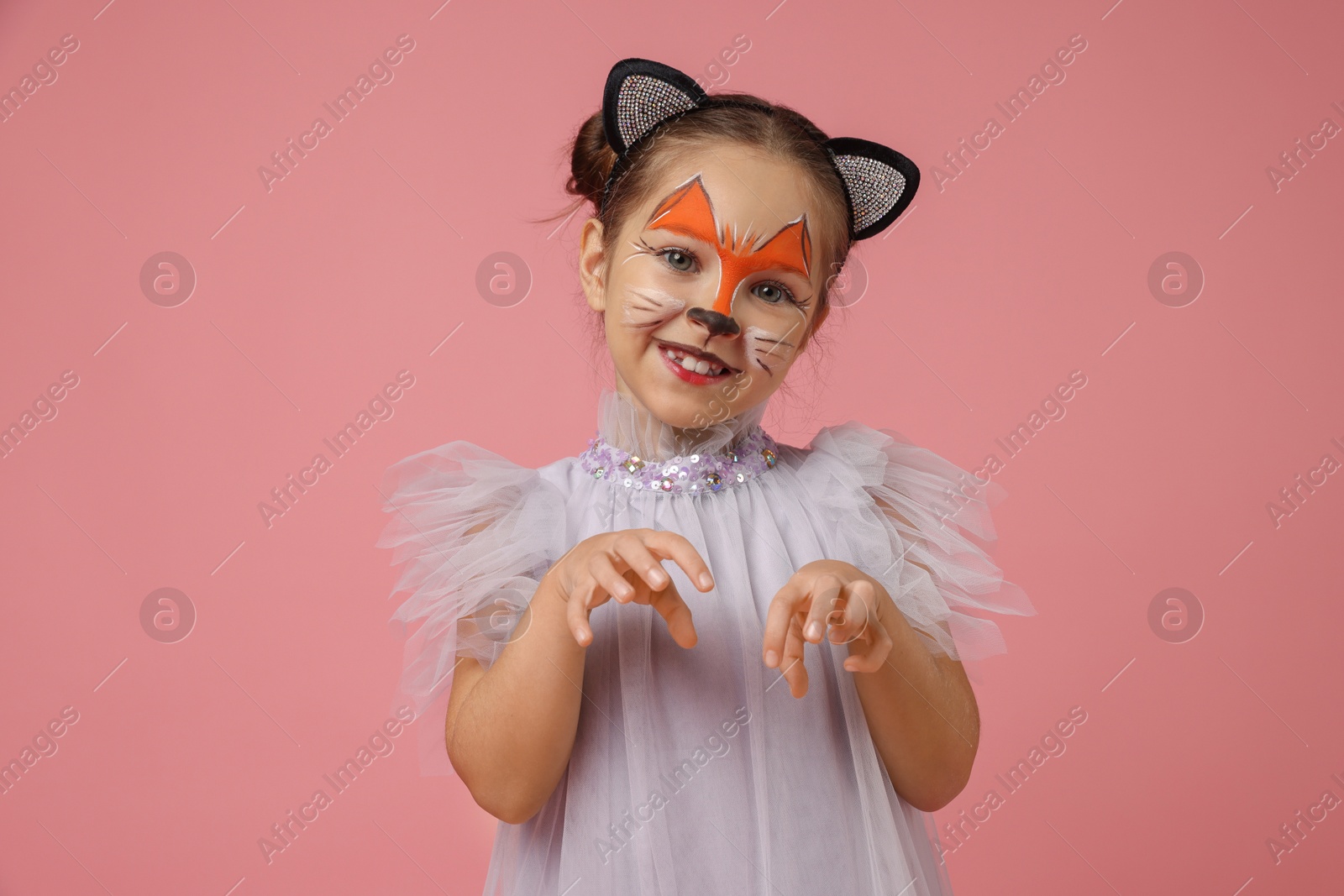 Photo of Cute girl with painted face and ears as cat on pink background