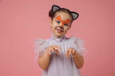 Cute girl with painted face and ears as cat on pink background